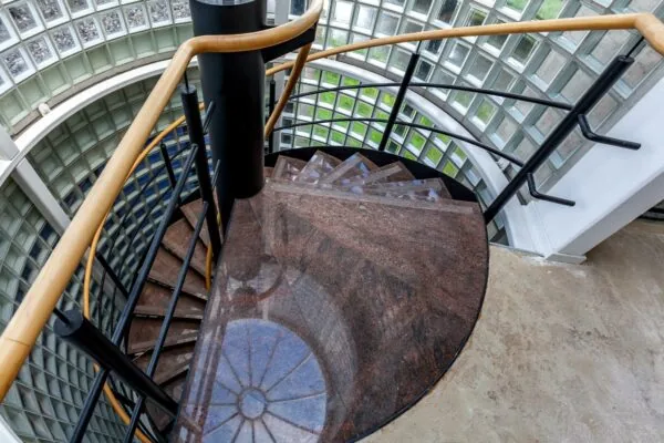 Wenteltrap met rode natuurstenen treden in een glazen trappenhuis aan de Rivium 1e Straat.